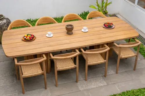 Contemporary Outdoor Wooden Dining Table with Eight Woven Armchairs, Tableware, Fresh Fruit Bowls, and Decorative Centerpiece in a Stylish Patio Garden Setting